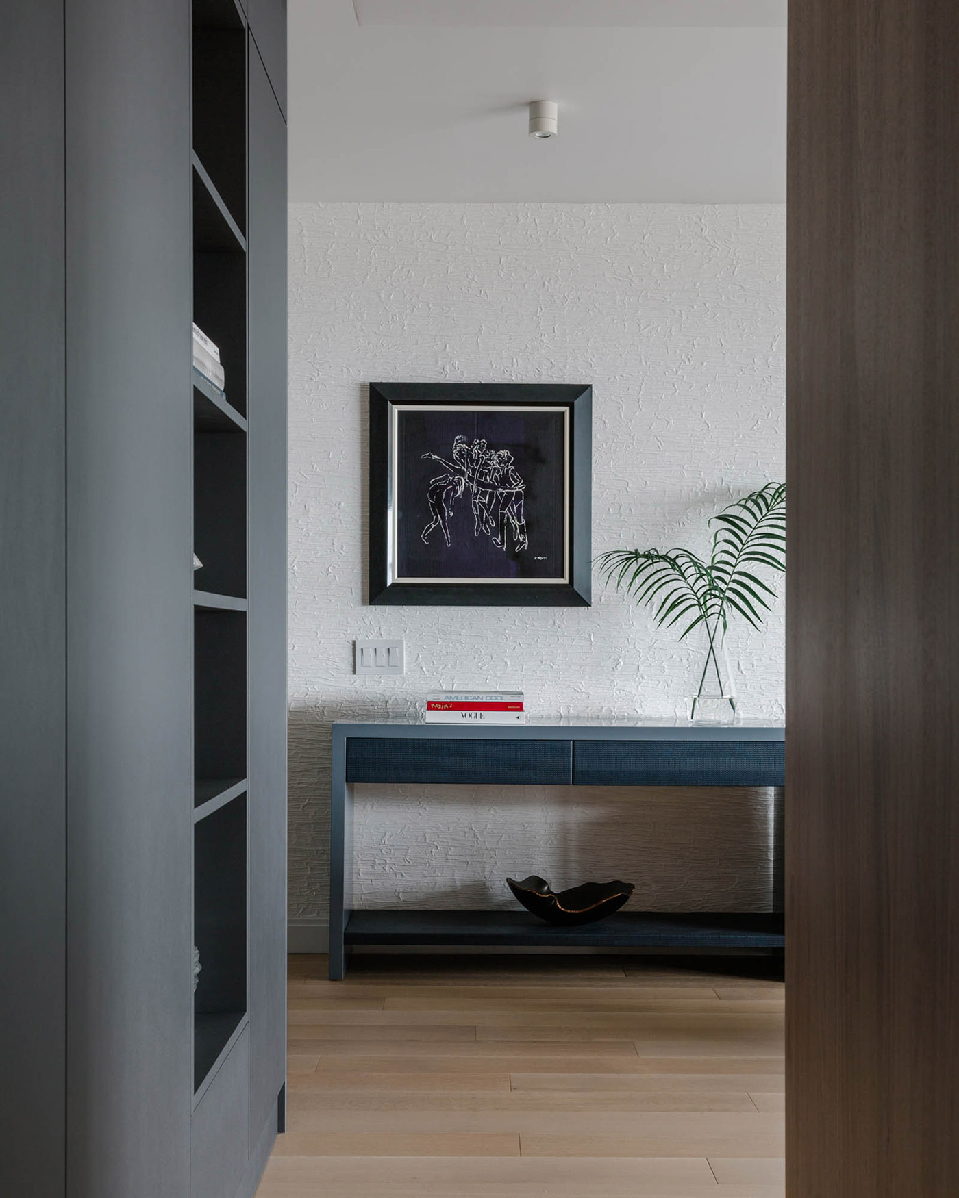 A hallway with a blue console table and dramatic black and white art.