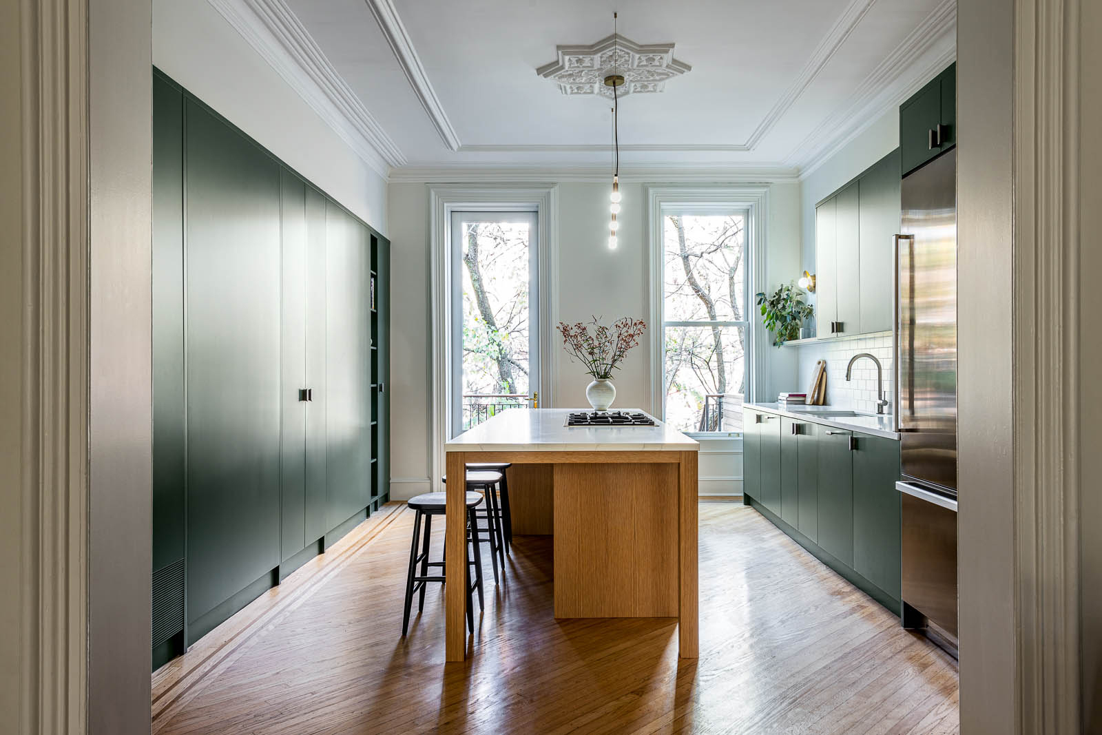 Green cabinetry and warm wood tones in a light-filled kitchen.